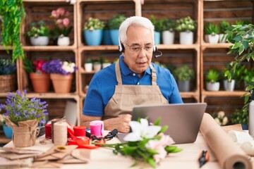 Middle age man with grey hair working at florist shop doing video call scared and amazed with open mouth for surprise, disbelief face