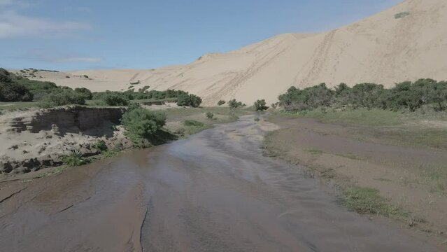 Close to the ground aerial shot of river in Llani, Chile where the sand dunes meet thhe grasslands
