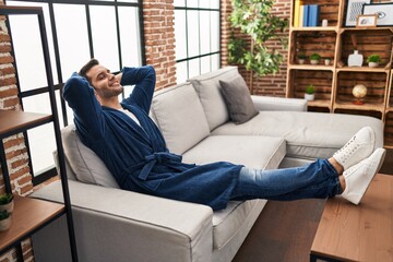 Young hispanic man wearing bathrobe relaxed with hands on head at home - obrazy, fototapety, plakaty