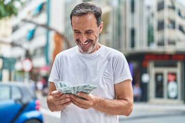 Middle age man smiling confident counting dollars at street