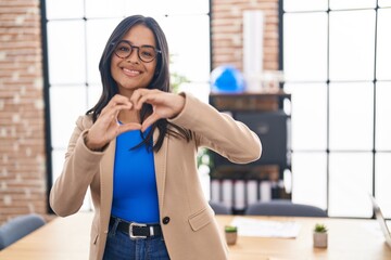 Brunette woman working at the office wearing glasses smiling in love showing heart symbol and shape with hands. romantic concept.