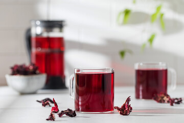 Herbal tea made from hibiscus petals in a transparent cup on a light background and a bowl of dry...