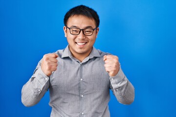 Young chinese man standing over blue background celebrating surprised and amazed for success with arms raised and open eyes. winner concept.