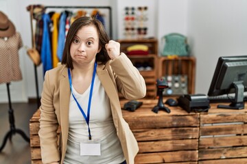 Young down syndrome woman working as manager at retail boutique angry and mad raising fist frustrated and furious while shouting with anger. rage and aggressive concept.