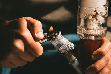 Close up of man smoking pot using lighter, medical marijuana or cannabis from a bong or water pipe....
