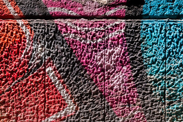 Colorful structures made by graffiti street artists on a stone wall close up. Details of sprayed abstract image in red, pink and turquoise on a facade of a house in Naples with bright side light.