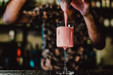 man hand bartender making pink cocktail in glass on the bar counter