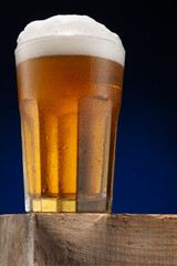 A large faceted glass full of beer with foam, a cold glass, with drops of sweat, on a wooden...