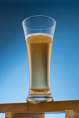 On a wooden stand a glass with beer or other drink, on a blue background, close-up