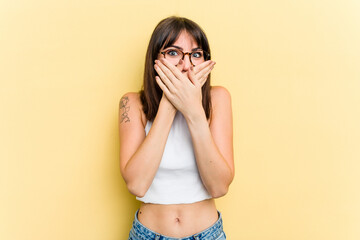 Young caucasian woman isolated on yellow background covering mouth with hands looking worried.