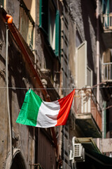 Italian flag in national colors green, white and red haging in a narrow street of old town of Naples. Tricolore blown by wind with facades of old houses with small balconys blurred in the background.