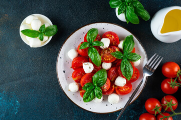 Italian caprese salad with sliced tomatoes, mozzarella, basil, olive oil on a dark background. Top view. Italian food. Healthy salad. Summer food