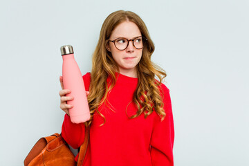 Young student woman holding a canteen isolated on blue background confused, feels doubtful and unsure. - obrazy, fototapety, plakaty