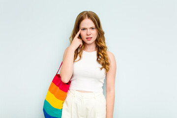 Young caucasian woman holding LGTBI bag isolated on blue background showing a disappointment gesture with forefinger.