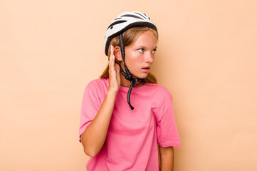 Little caucasian girl wearing a bike helmet isolated on beige background trying to listening a gossip.