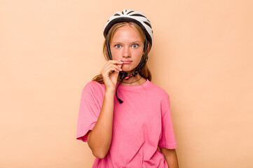 Little caucasian girl wearing a bike helmet isolated on beige background with fingers on lips keeping a secret.