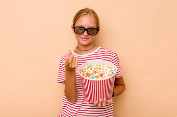 Obraz premium Little caucasian girl eating popcorn isolated on beige background pointing with finger at you as if inviting come closer.