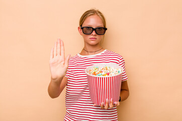 Little caucasian girl eating popcorn isolated on beige background standing with outstretched hand...