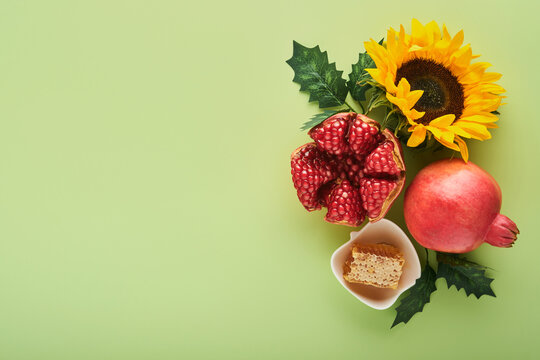 Rosh Hashanah. Ripe pomegranate, apple, honey and sunflower, yellow flowers on green background. composition with symbols jewish Rosh Hashanah holiday attributes. Top view with copy space.