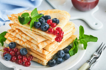 Pancakes. Stack of crepes or thin pancakes with berries, blueberries, red currants, raspberries and honey for breakfast. Homemade breakfast. Copy space. Selective focus.