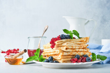 Pancakes. Stack of crepes or thin pancakes with berries, blueberries, red currants, raspberries and honey for breakfast. Homemade breakfast. Copy space. Selective focus.