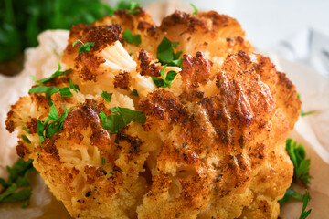 Baked cauliflower. Oven or whole baked cauliflower spices and herbs server on wooden rustic board on old white wooden background table. Delicious cauliflower. Eyal Shani dish. Perfect tasty snack.