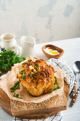 Baked cauliflower. Oven or whole baked cauliflower spices and herbs server on wooden rustic board on old white wooden background table. Delicious cauliflower. Eyal Shani dish. Perfect tasty snack.