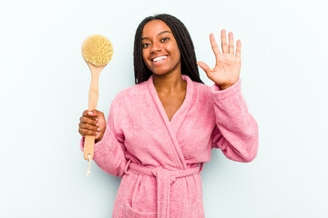 Young African American woman holding a bathtub brush isolated on blue background smiling cheerful showing number five with fingers.