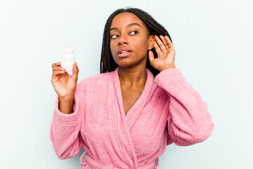 Young African American woman wearing bathrobe holding a deodorant isolated on blue background...