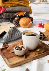 Cozy autumn composition, sweater weather. Hot tea with lemon and nuts on wooden tray surrounded with autumn leaves and sweaters