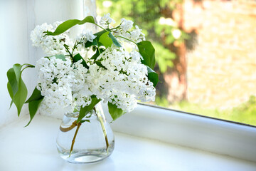 Bouquet of white lilac in glass vase on white window sill Copy space