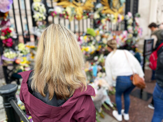 Woman stands in front of flowers at Buckingham Palace in London UK to mourn the death of Queen Elizabeth II.