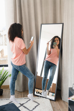 Vertical portrait of young african woman student taking selfie looking at the mirror at home, preparing for date, blogging vlogging for social media online