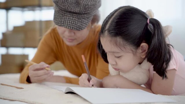 Sibling drawing book together on bed, elder sister and adorable little girl enjoying hobby pastime alone without parents in bedroom. Nanny teaching children draw in holiday, using colorful pencils

