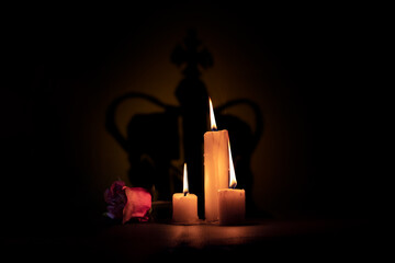 
lit candles next to a rose on a black background with a projected shadow of a crown representing...