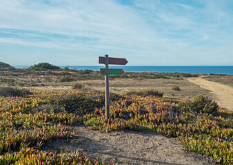 Signpost pointing the way on Praia do Sissal with the colours of Rota Vicentina Route and Fishermans trail beautiful hiking route that mixes sandy beaches, cliffs and vegetation. Porto Covo, Portugal