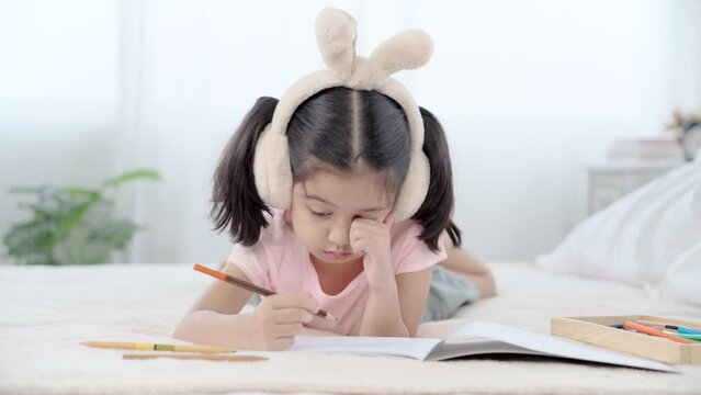 Adorable girl sleepy while drawing on book, Cute primary school age girls drawing coloring picture with pencils on bed in holiday. children development at home concept. 
