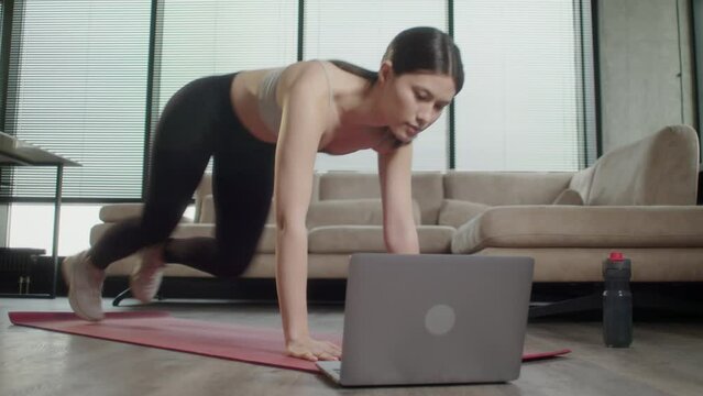 Cheerful active asian woman doing fitness at home, using laptop, watching online lessons. Positive well-fit lady in sportswear exercising during covid-19 pandemic, watching fitness videos on Internet