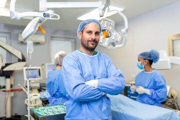 Portrait of male surgeon standing with arms crossed in operation theater at hospital. Team surgeons...