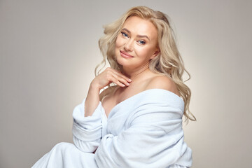 Caucasian mature blonde woman with a clean a healthy skin, wearing in spa bathrobe over grey...