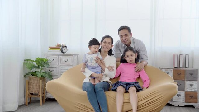 Happy family sitting on sofa and posing for photo, looking at camera, mother and father with two little baby enjoying tender moment together. house takea photo together in holiday at home.

