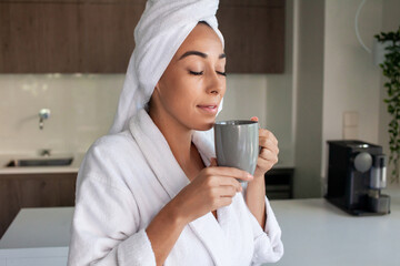 Contented woman drinking tea at home. Woman in bathrobe sitting in kitchen, holding cup. Home, morning routine concept