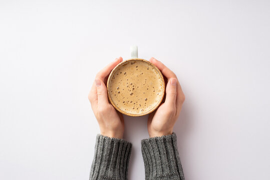 Autumn concept. First person top view photo of female hands in grey sweater holding cup of hot drinking on isolated white background