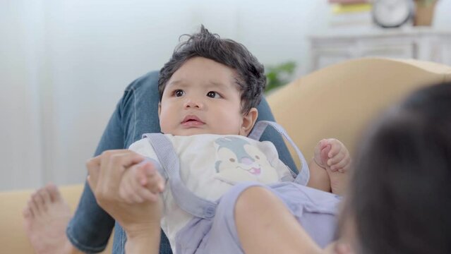 Asian cute infant sitting on mother lap after wake up and enjoy with her tease. Healthy relax mom play with newborn baby in living room, toddler little boy having fun and happy nuturing motherhood
