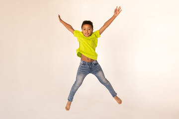 Portrait of happy preteen boy jumping against white background. Excited mixed race child wearing green T-shirt and jeans having fun. Happiness concept