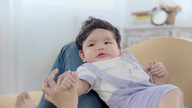 Asian cute infant sitting on mother lap after wake up and enjoy with her tease. Healthy relax mom play with newborn baby in living room, toddler little boy having fun and happy nuturing motherhood
