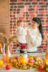 A young mother and little daughter in white warm knitted sweaters in an interior decorated with blankets and pillows
 as well as pumpkins, autumn leaves and apples. Autumn mood. halloween