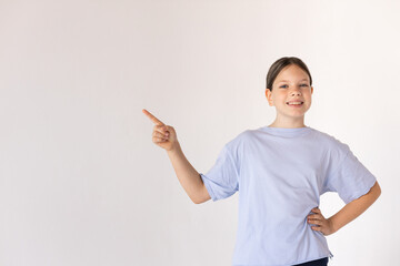 Portrait of happy preteen girl showing something. Caucasian child wearing blue T-shirt standing and smiling against white background. Presentation and education concept