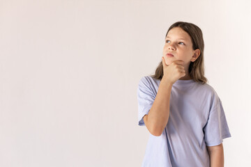 Portrait of pensive preteen girl looking away. Caucasian child wearing blue T-shirt thinking rubbing her chin against white background. Dreaming concept