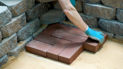 Closeup of a womans hand installing brick pavers onto a sand base for a patio construction.